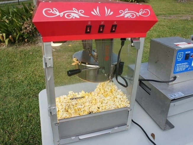 Aparat de popcorn cu acoperiș roșu și cuvă transparentă cu popcorn, în exterior.