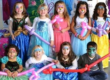 Grup de copii în costume de poveste ținând baloane lungi modelate, inclusiv săbii și figurine.